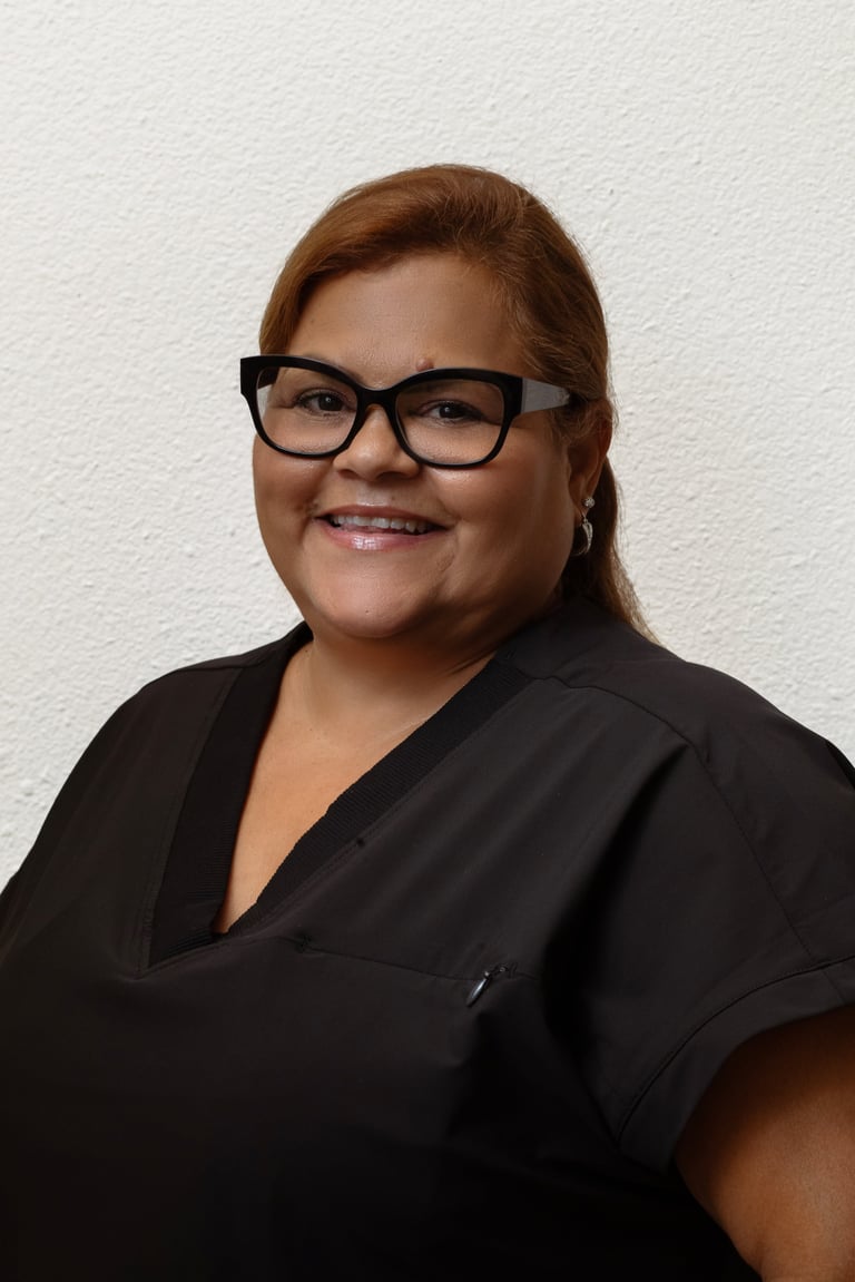 Professional headshot of a woman with reddish-brown hair, black-framed glasses, and a black shirt, smiling at the camera against a white background.