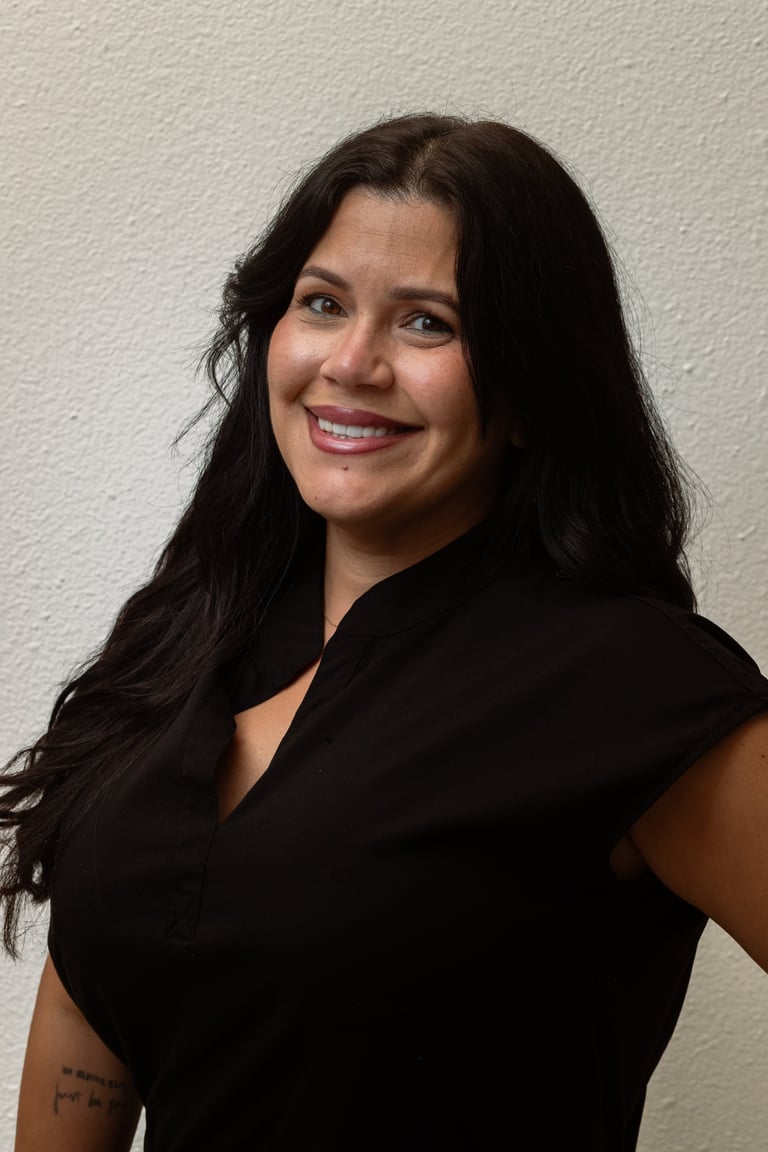 Woman with long dark hair smiling at the camera, wearing a black sleeveless top against a light gray background