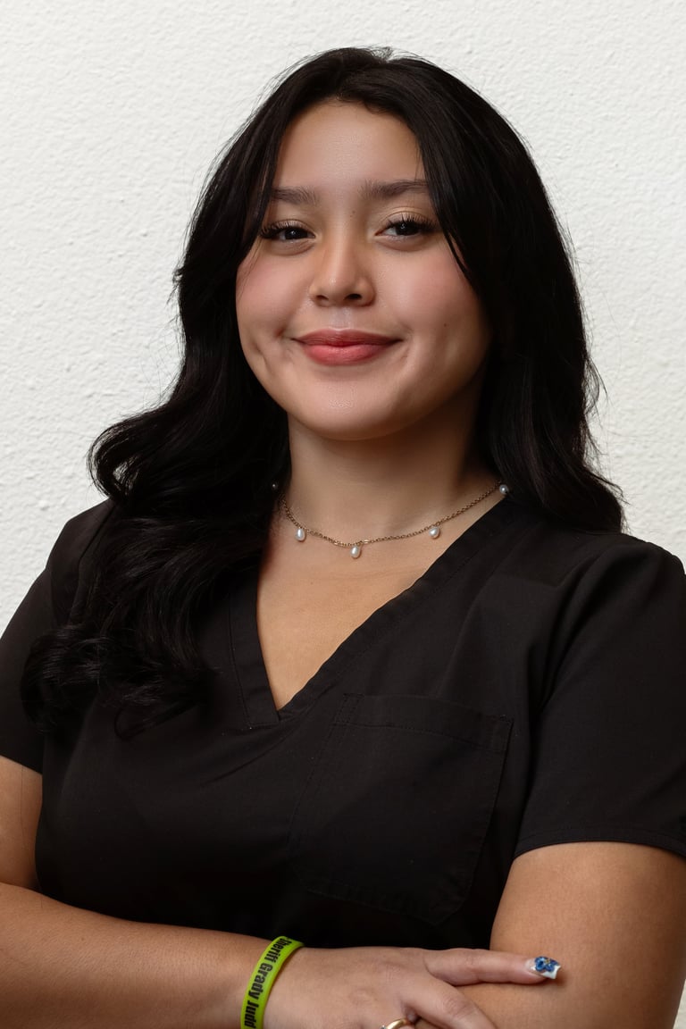 Woman with long black hair wearing black v-neck top and delicate necklace, smiling at camera against white background