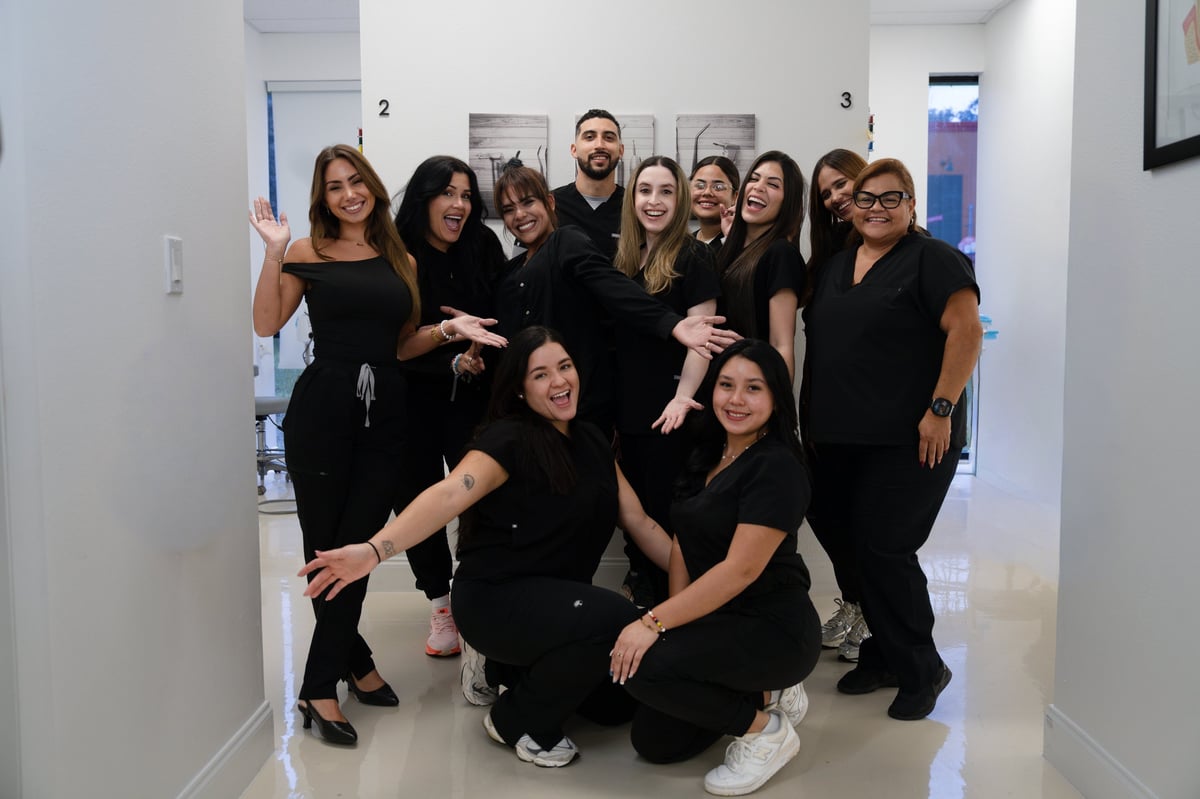 A group of twelve women in black outfits posing together in a modern office hallway, smiling at the camera.