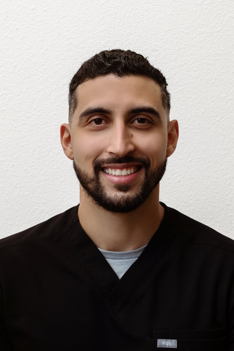 Headshot of a smiling man with dark hair and beard wearing a black shirt against a white background