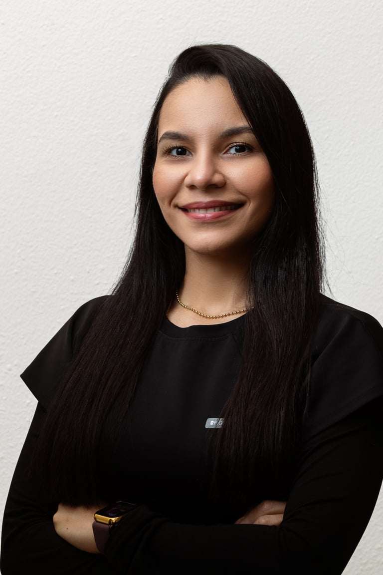 Portrait of a young woman with long black hair wearing a black top, smiling at the camera with arms crossed