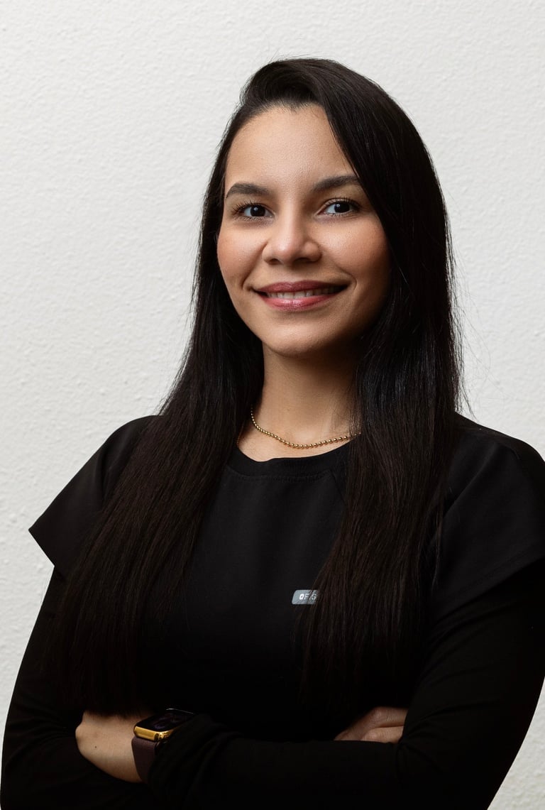 Professional headshot of a smiling woman with long black hair wearing a black shirt and gold accessories against a white background