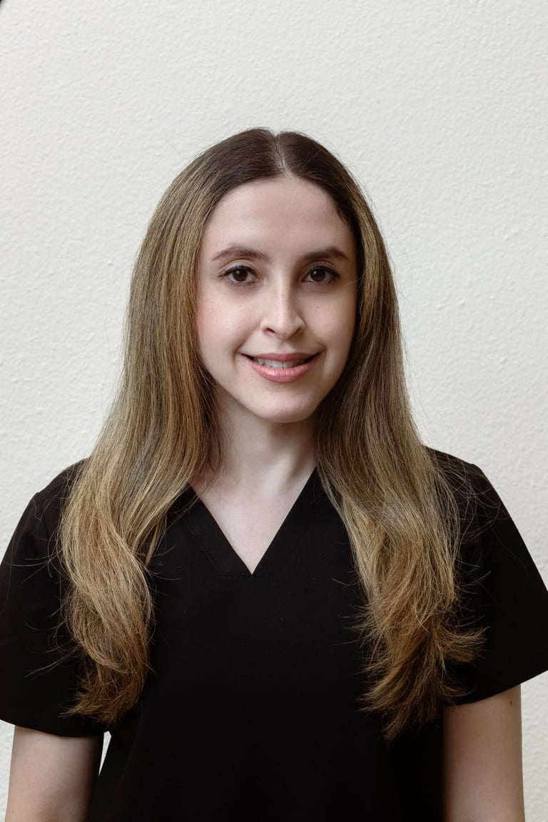 Portrait of a young woman with long brown hair smiling at the camera, wearing a black v-neck shirt against a plain white background