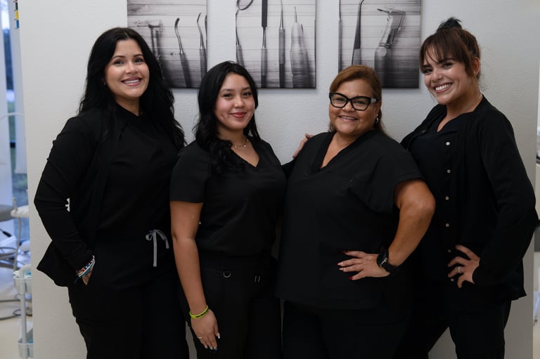 Four women in black professional attire smiling at the camera in an office setting
