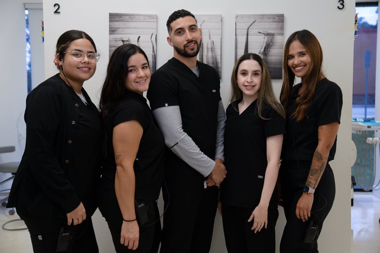 Five professionals in black attire standing together and smiling inside a modern office space