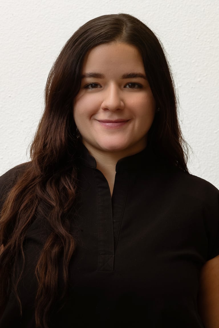 Professional headshot of a young woman with long brown hair wearing a black shirt against a white background