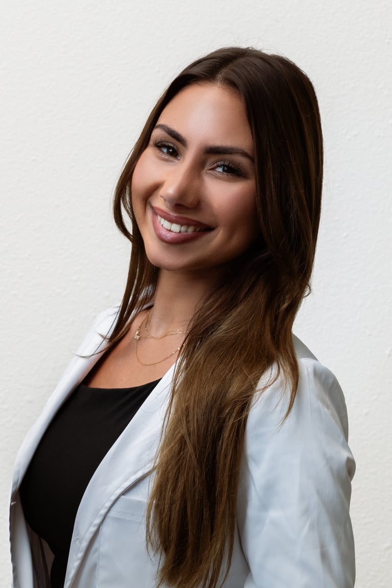 Professional headshot of a smiling woman with long dark hair wearing a white blazer over a black top